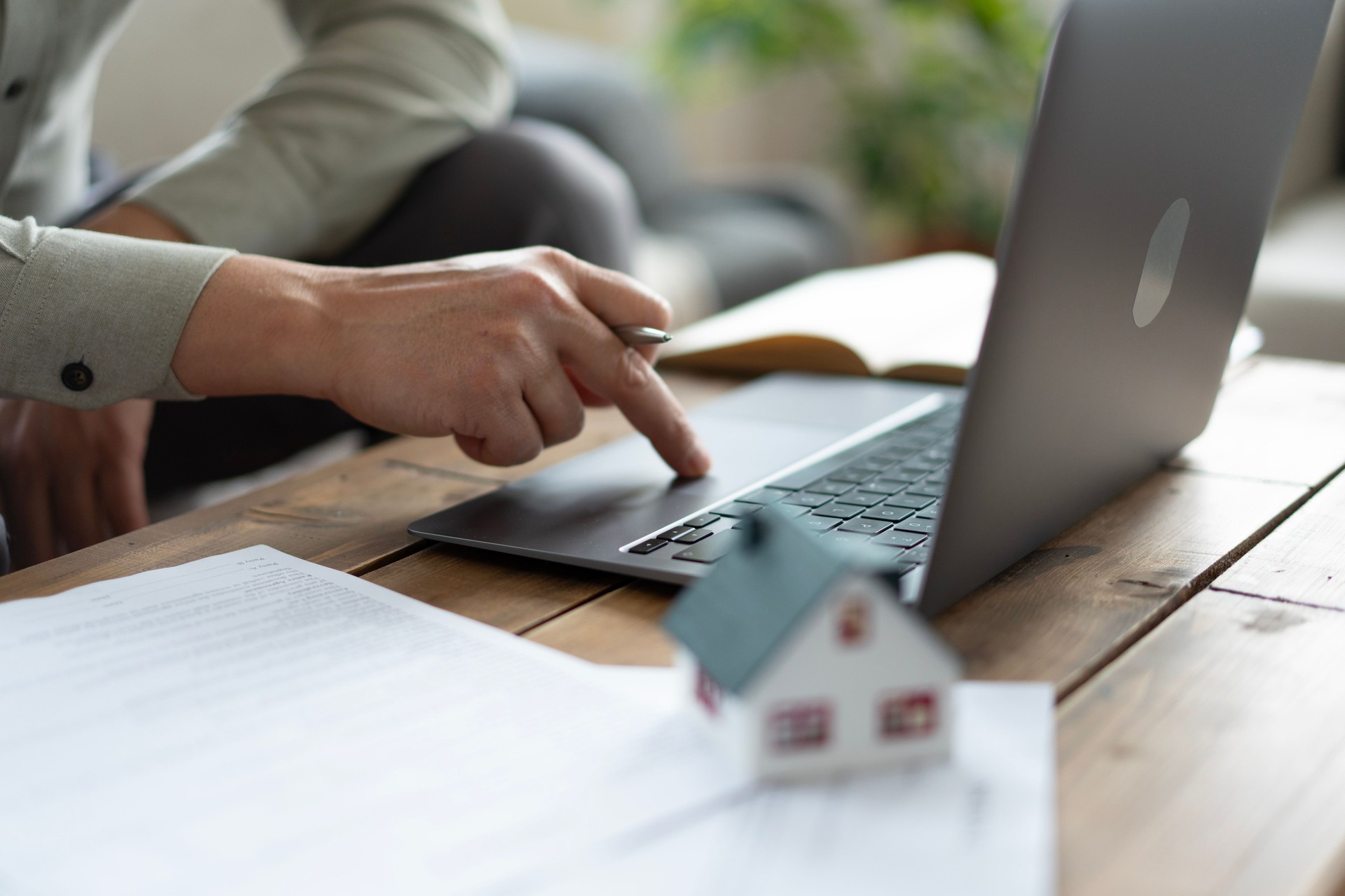 Real estate agent browsing listings on laptop with miniature house